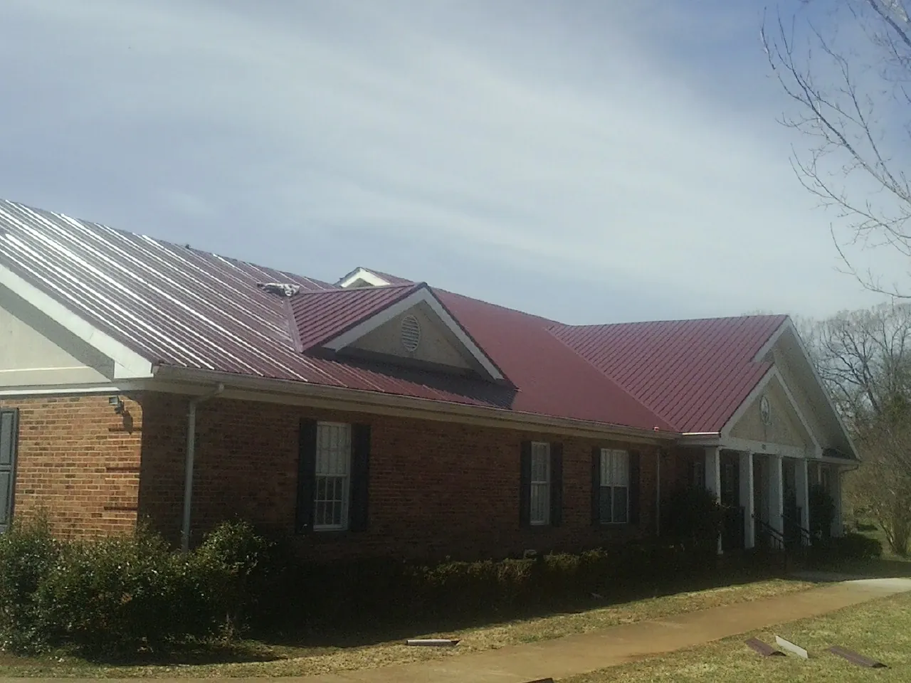 Red metal roof with gabled entries on a long brick building, from a Hail Damage Roof Repair job in Plattsmouth