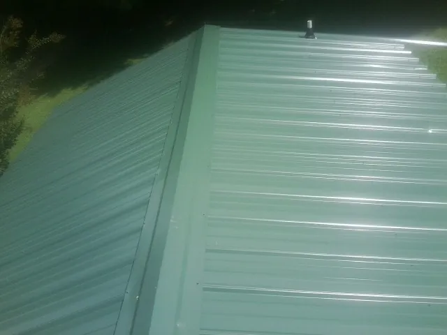 New green metal panels meeting at the ridge of a roof — Flat Roof Repair work by our crew in Plattsmouth