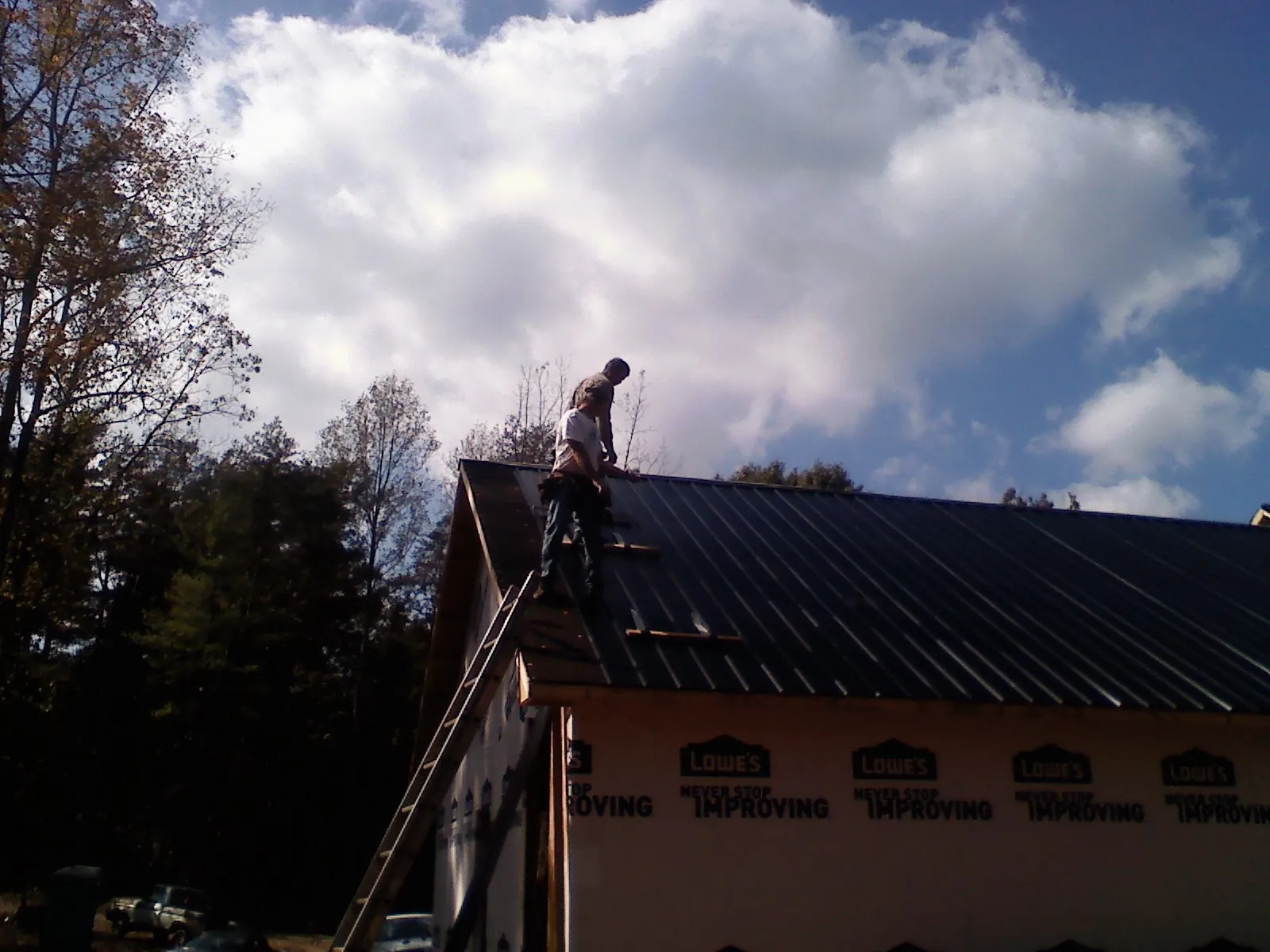 Roofer fastening dark metal panels high against a cloudy sky, from a Roof Inspection job in Plattsmouth
