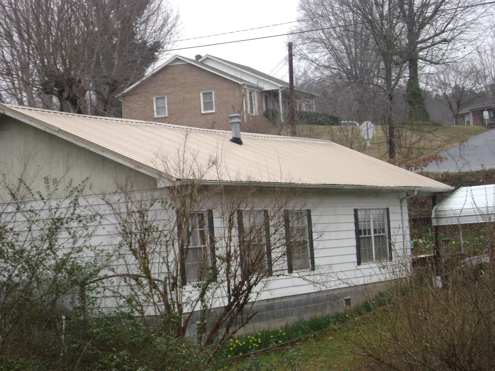 Tan metal roof on a white sided house set into a hillside — Commercial Roofing by Roofing Brothers in Plattsmouth